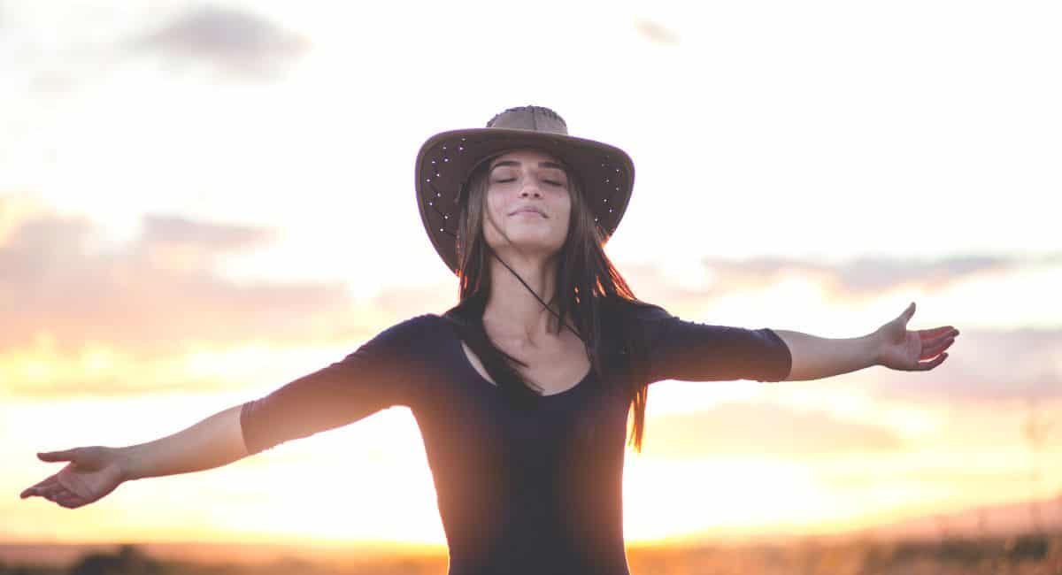 gorgeous woman in a brown hat spreading her two hands and feeling the breeze